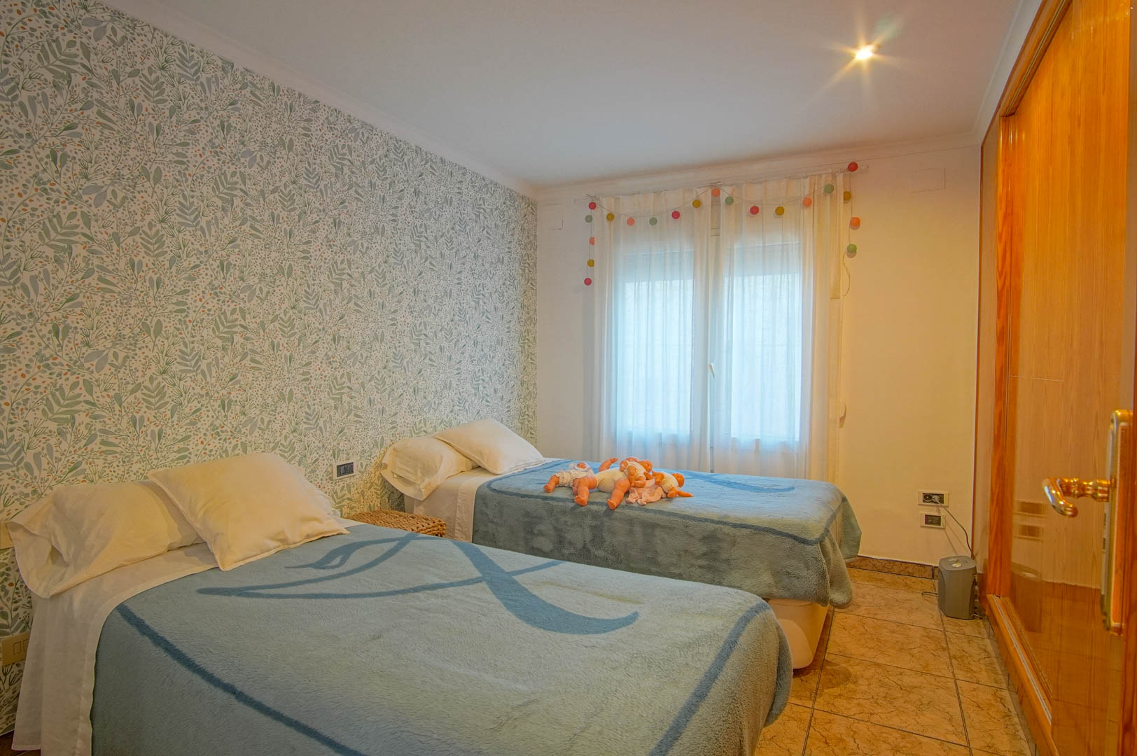 Chambre à coucher avec lits jumeaux, mur d'accent au motif végétal, placard intégré en bois et sol en carrelage clair.
