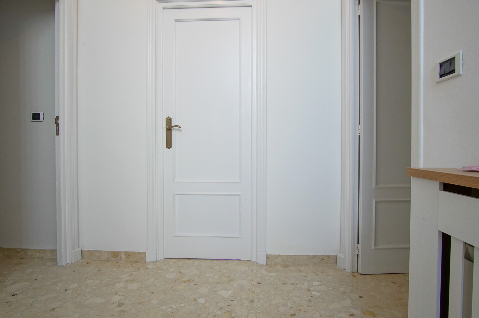 Couloir intérieur avec des portes laquées blanches à panneaux et un sol en marbre poli. Les finitions incluent des moulures classiques et une quincaillerie en laiton.