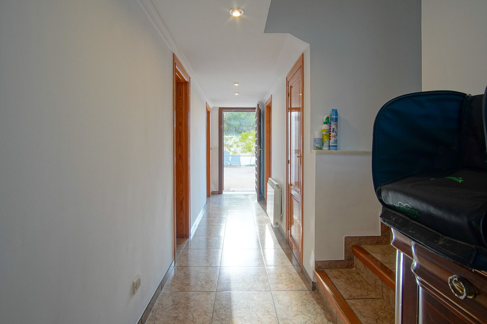 Couloir lumineux avec sol en grès cérame et cadres de portes en bois, offrant un accès direct vers la terrasse extérieure et l'escalier latéral.