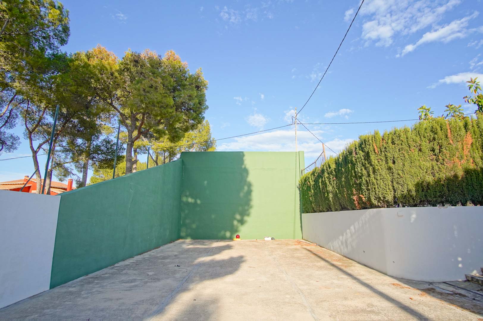 Court de fronton privé avec murs verts et sol en béton, entouré de pins matures et de haies hautes assurant une discrétion totale.