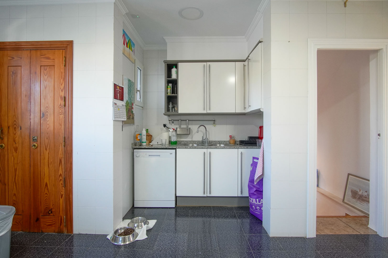 Cuisine fonctionnelle de l'appartement d'invités avec meubles blancs, plan de travail en granit et sol en terrazzo foncé, située près de l'accès aux étages.