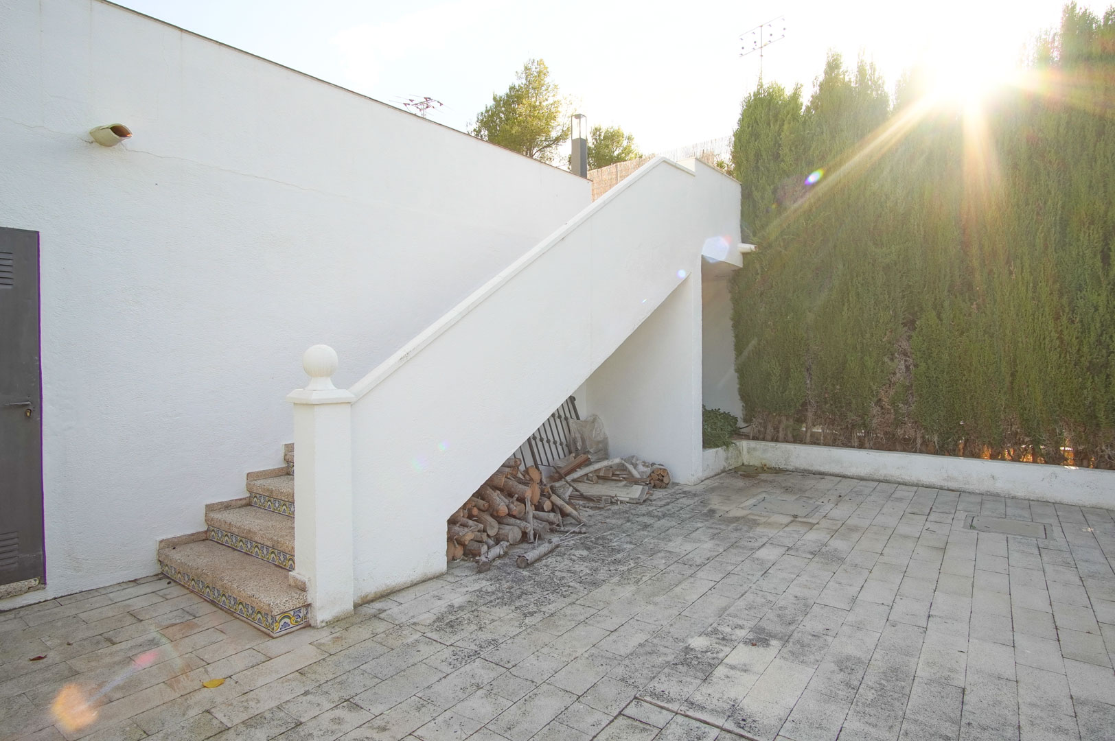 Escalier extérieur en pierre avec contremarches en céramique décorative, donnant sur un patio pavé bordé d'une haie de cyprès protectrice.