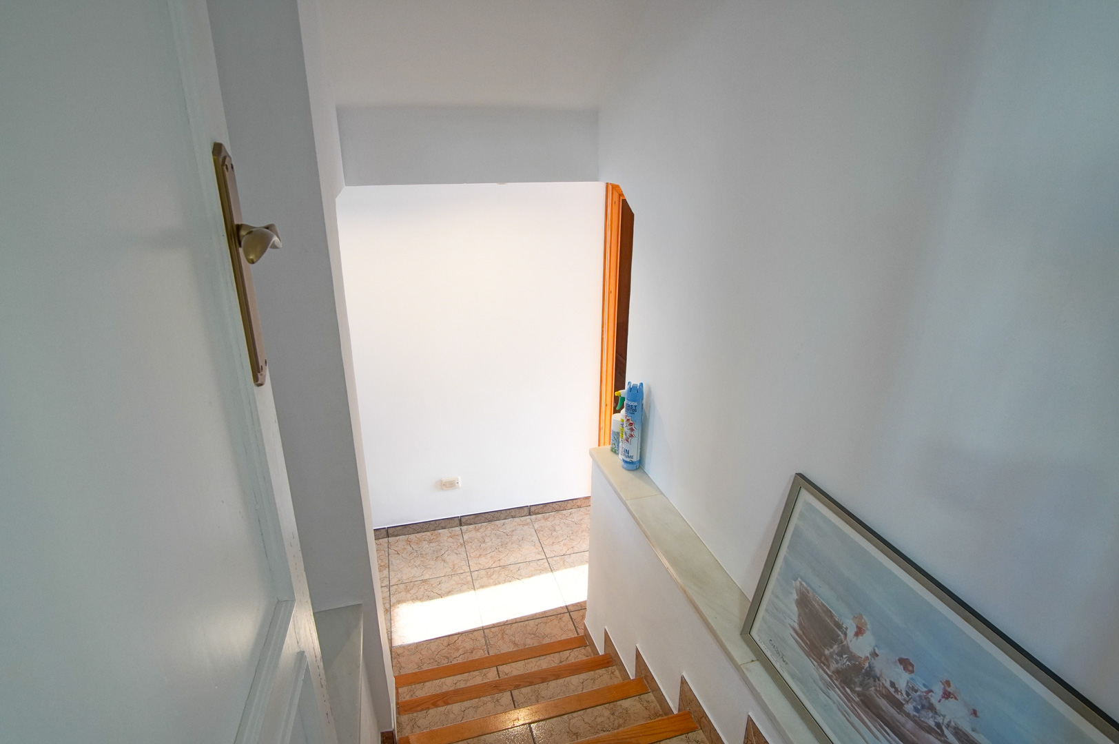 Escalier intérieur alliant bois et céramique, offrant un passage lumineux vers les niveaux inférieurs grâce à ses murs blancs et sa lumière naturelle.