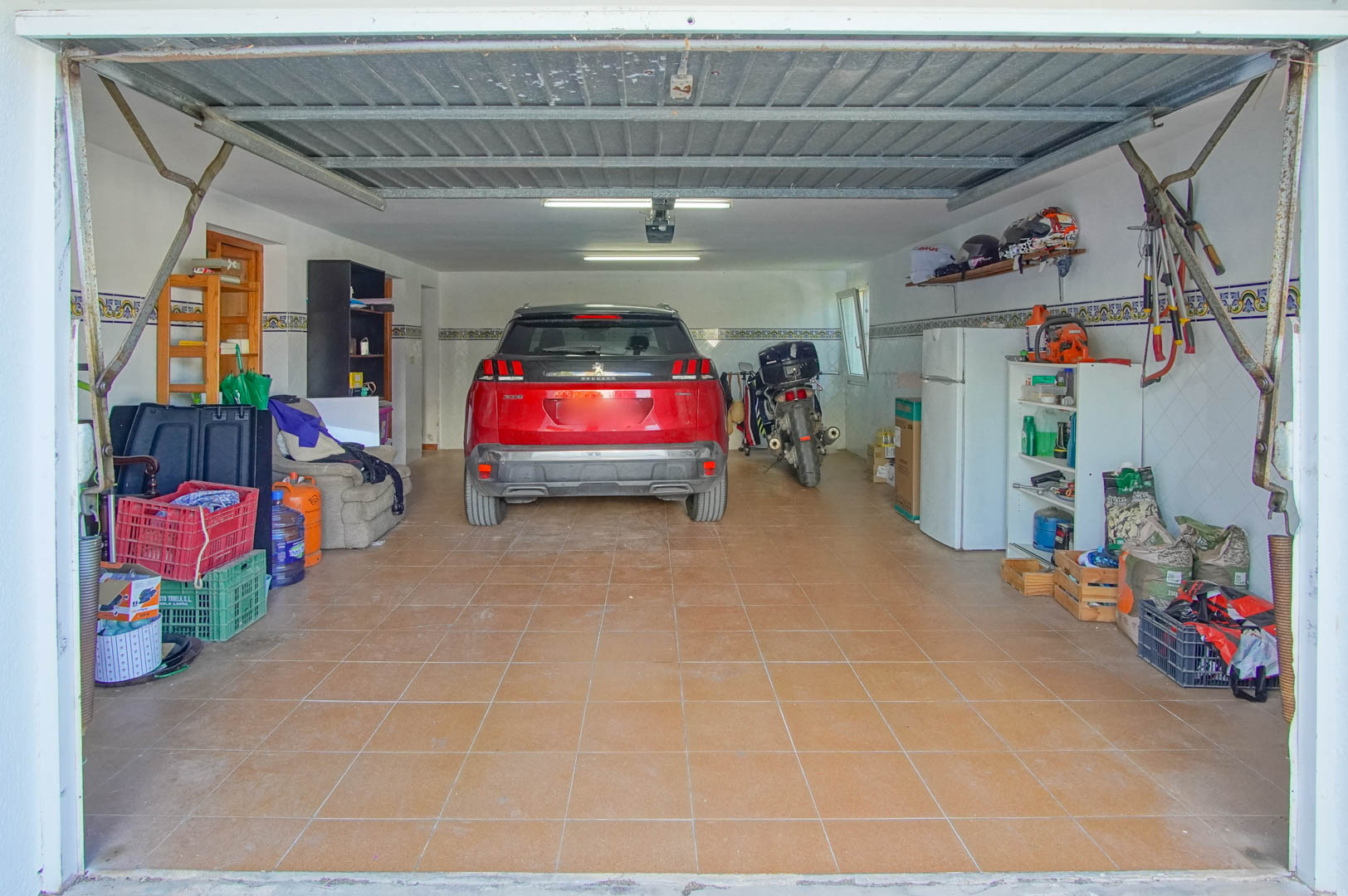 Garage fermé en demi-sous-sol avec sol en céramique, éclairage fluorescent et espace fonctionnel pour véhicules et stockage d'outillage.