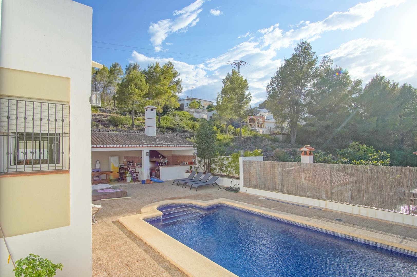 Piscine privée avec grande terrasse en pierre, cuisine d'été couverte et vue sur les collines boisées du parc naturel du Montgó.