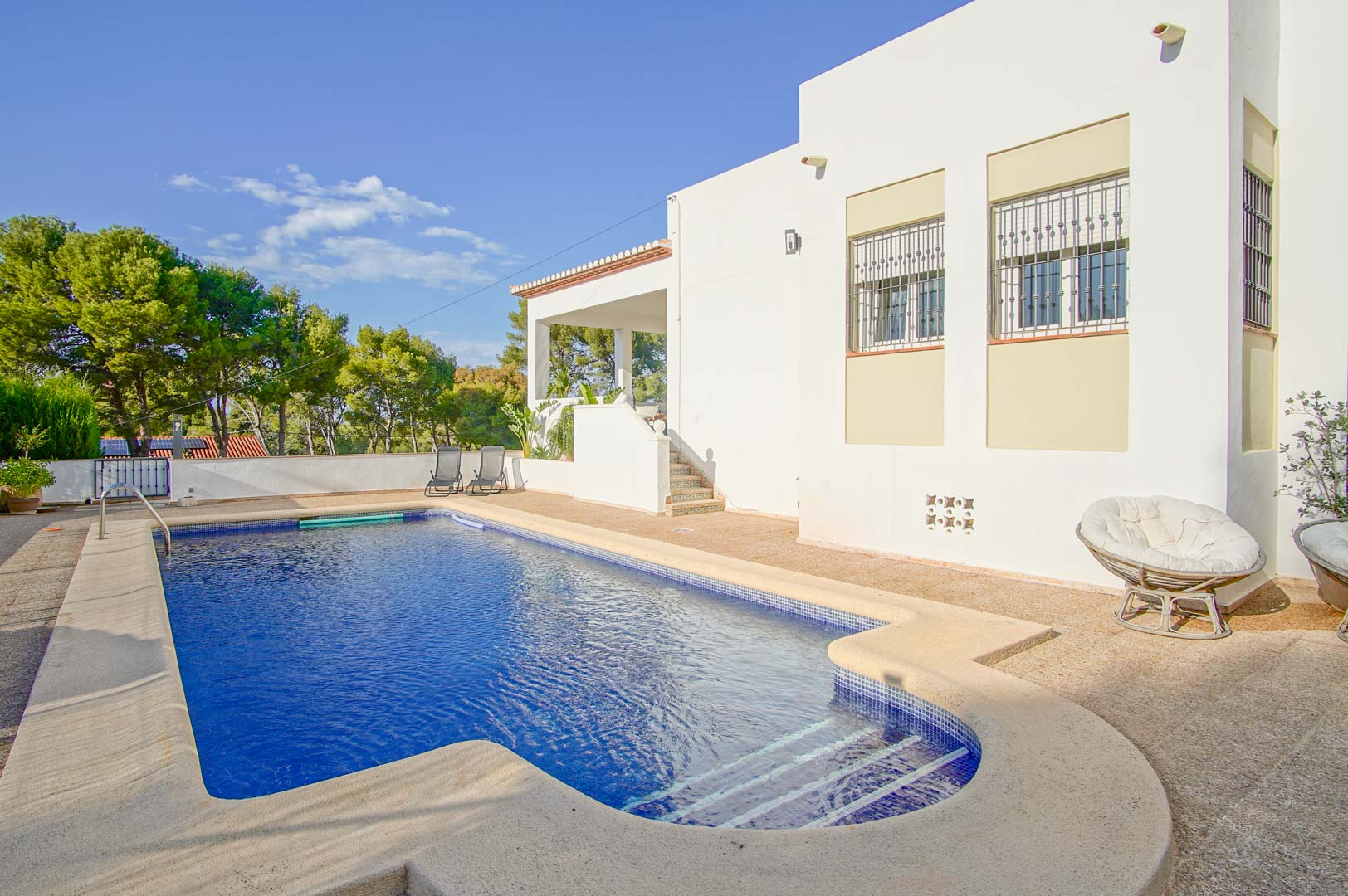 Piscine privée avec mosaïque bleue et terrasse en pierre, située devant la façade blanche de la villa et entourée d'une pinède méditerranéenne.