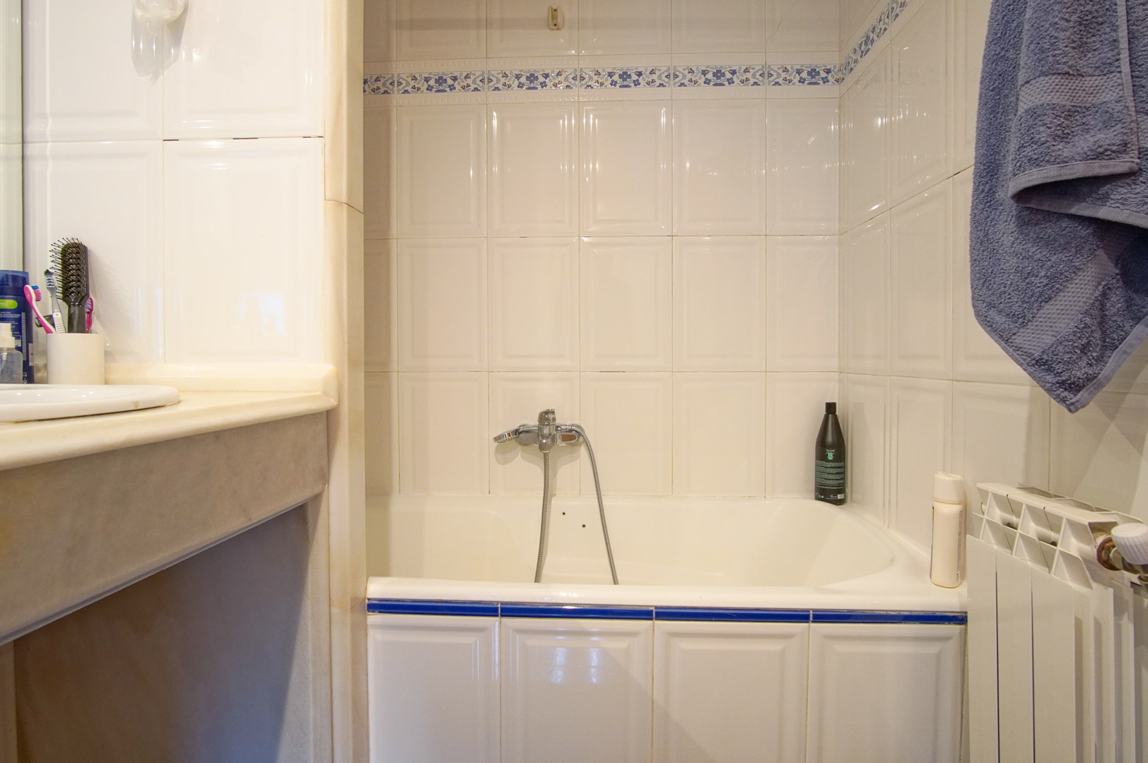 Salle de bain avec baignoire, carrelage blanc à motifs floraux bleus et plan de vasque en marbre. Équipée d'un radiateur blanc et d'une robinetterie chromée.