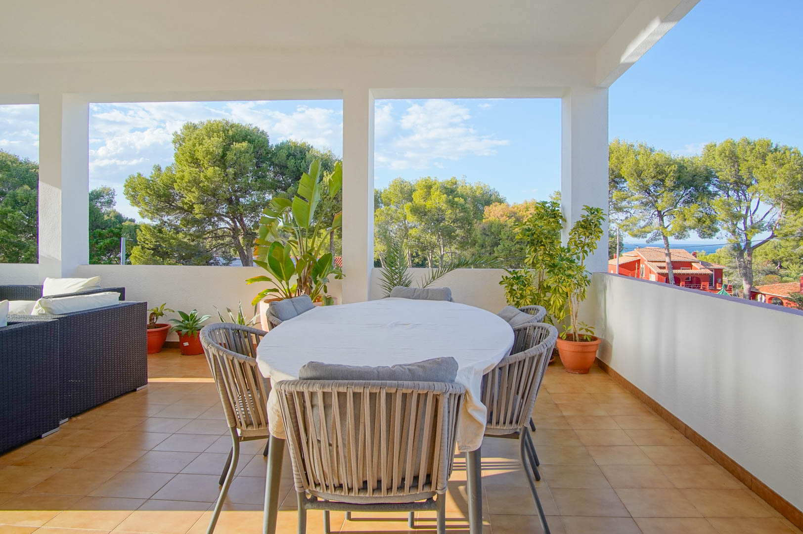 Terrasse couverte avec coin repas et salon de jardin, offrant une vue dégagée sur la forêt de pins méditerranéenne et l'horizon marin de Dénia.