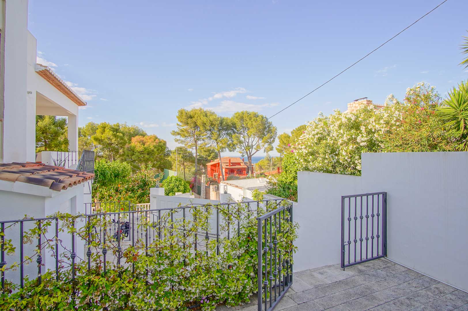 Vue depuis la terrasse en pierre avec garde-corps en fer forgé, surplombant un jardin méditerranéen avec un aperçu sur la mer et les pinèdes environnantes de Las Rotas.