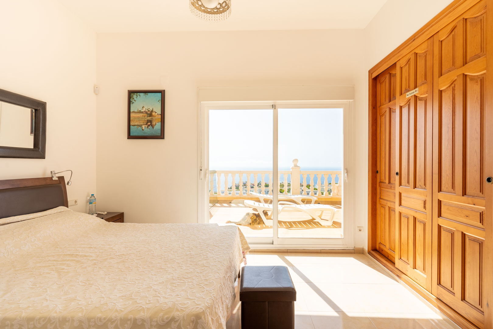 Chambre avec placards intégrés en bois et accès direct par une baie vitrée à une terrasse ensoleillée offrant une vue sur la mer.