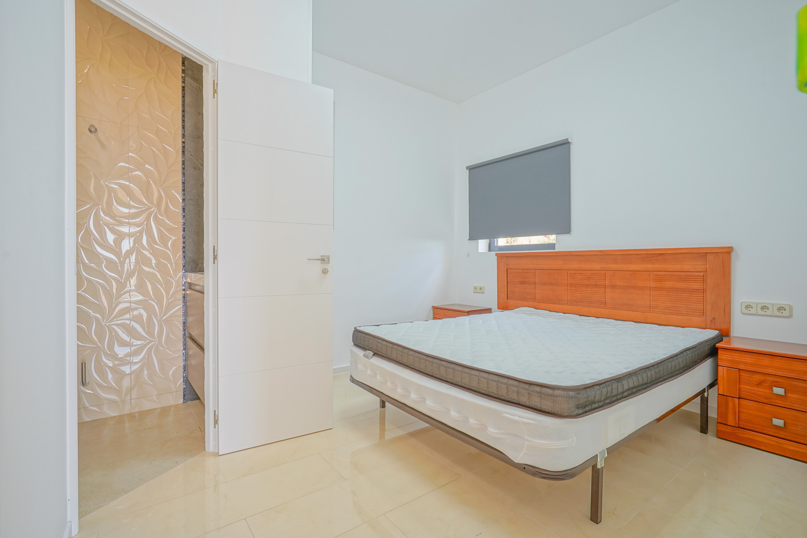 Chambre double avec mobilier en bois, sol en grès cérame clair et salle de bain attenante ornée de carreaux muraux à motifs texturés.