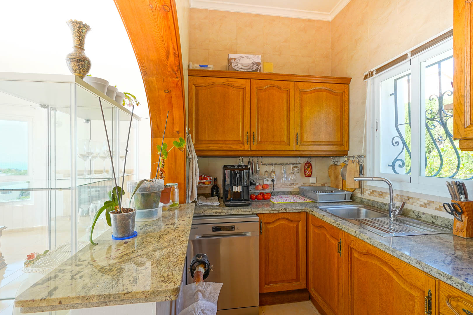 Cuisine semi-ouverte avec des meubles en bois classique, des plans de travail en granit et un évier en inox, le tout encadré par une arche en bois massif.