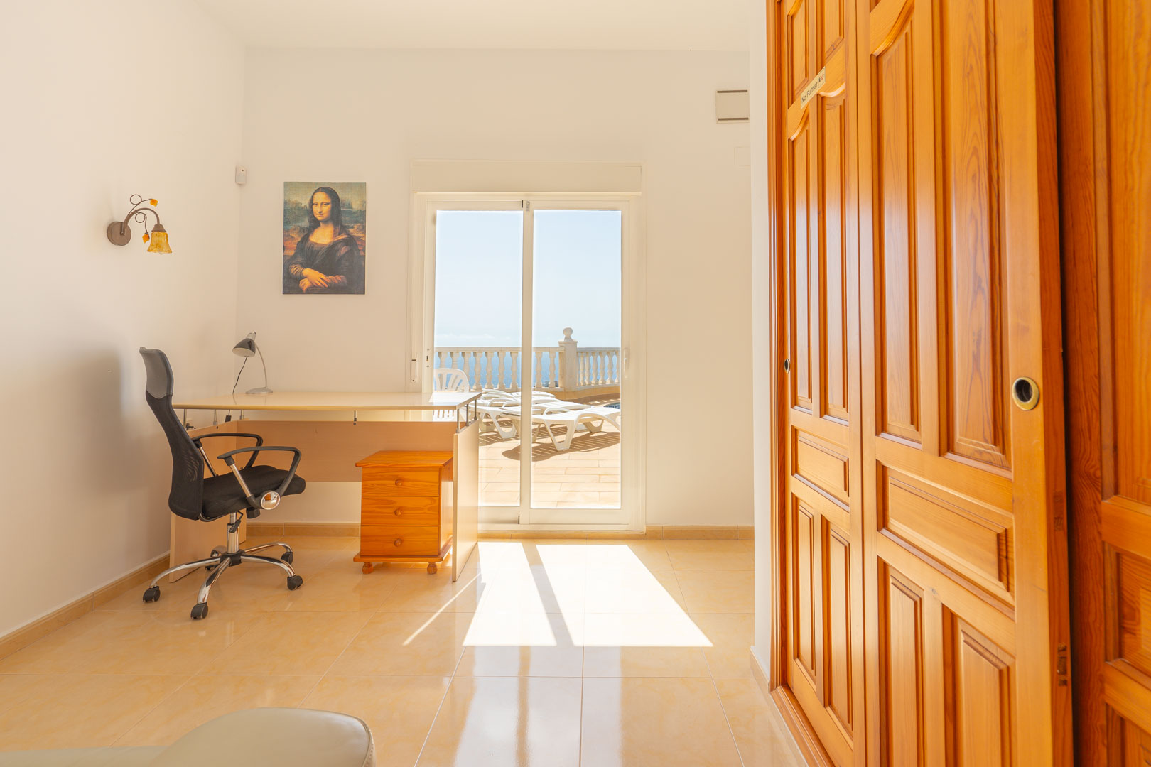 Pièce polyvalente avec espace bureau, placards intégrés en bois et accès direct à la terrasse ensoleillée offrant une vue sur la mer Méditerranée.