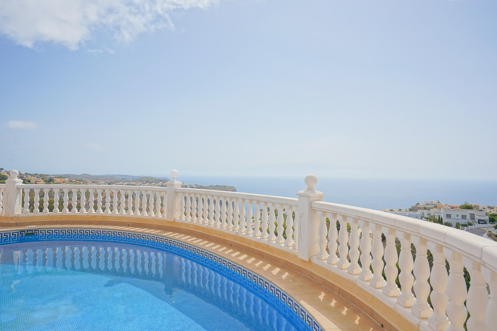 Piscine incurvée avec mosaïque bleue et frise grecque, bordée d'une balustrade blanche offrant une vue panoramique sur la mer Méditerranée.