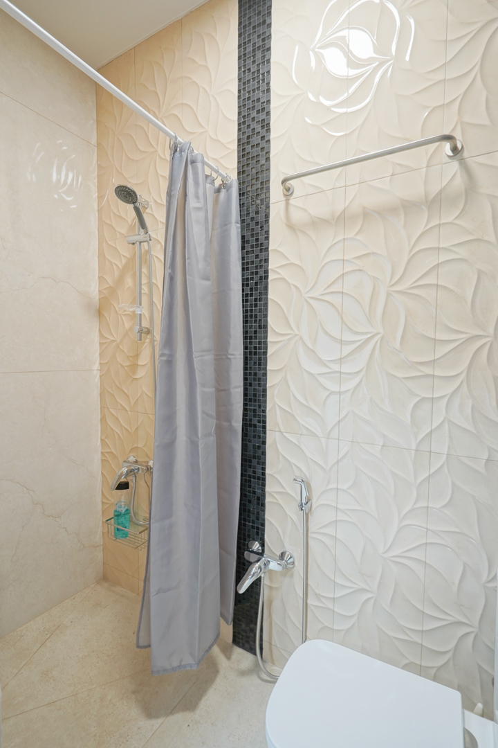 Salle de bain avec carrelage à relief floral, bande verticale en mosaïque noire et robinetterie chromée avec douchette à main.