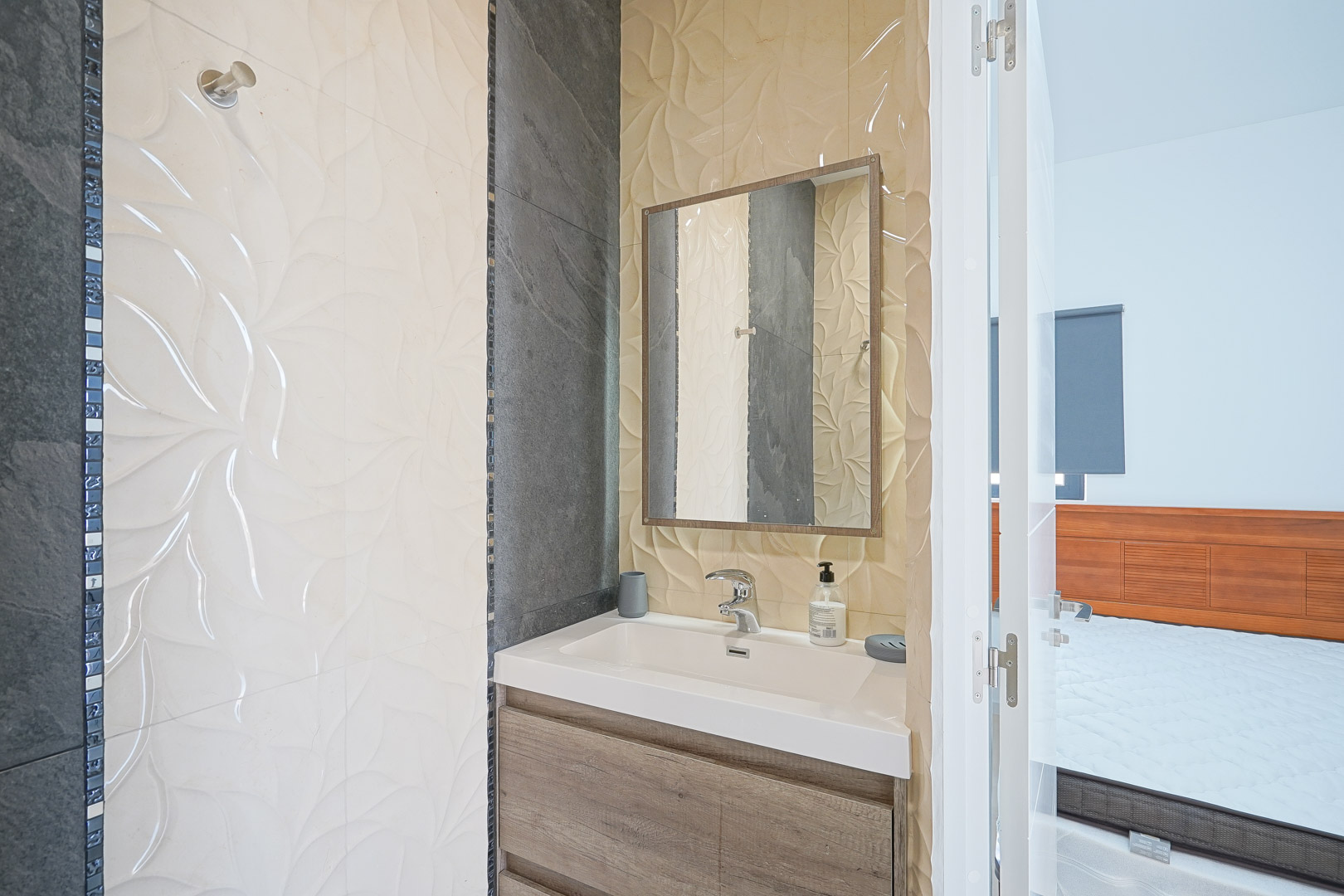 Salle de bains attenante avec meuble sous-vasque en bois, vasque intégrée et murs en carrelage texturé à motifs floraux et ardoise.