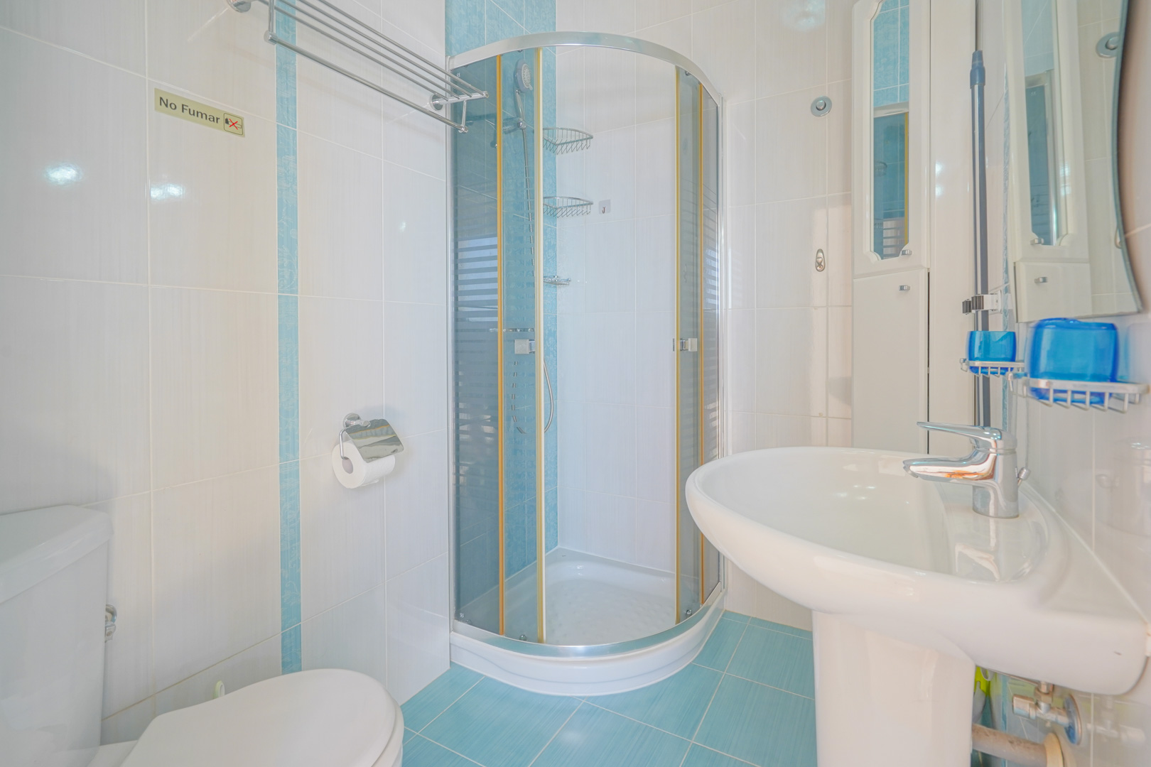 Salle de bains fonctionnelle avec carrelage blanc et bleu, cabine de douche d'angle arrondie et lavabo sur colonne blanc.