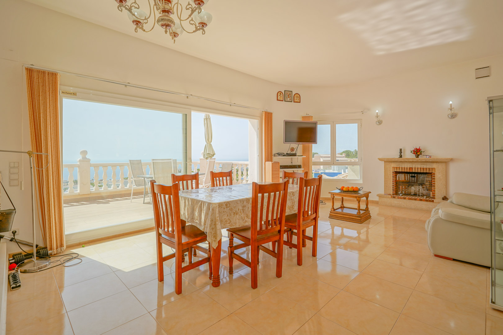 Salon-salle à manger lumineux avec cheminée en pierre, sol en céramique et grandes baies vitrées offrant un accès direct à la terrasse avec vue sur la mer.