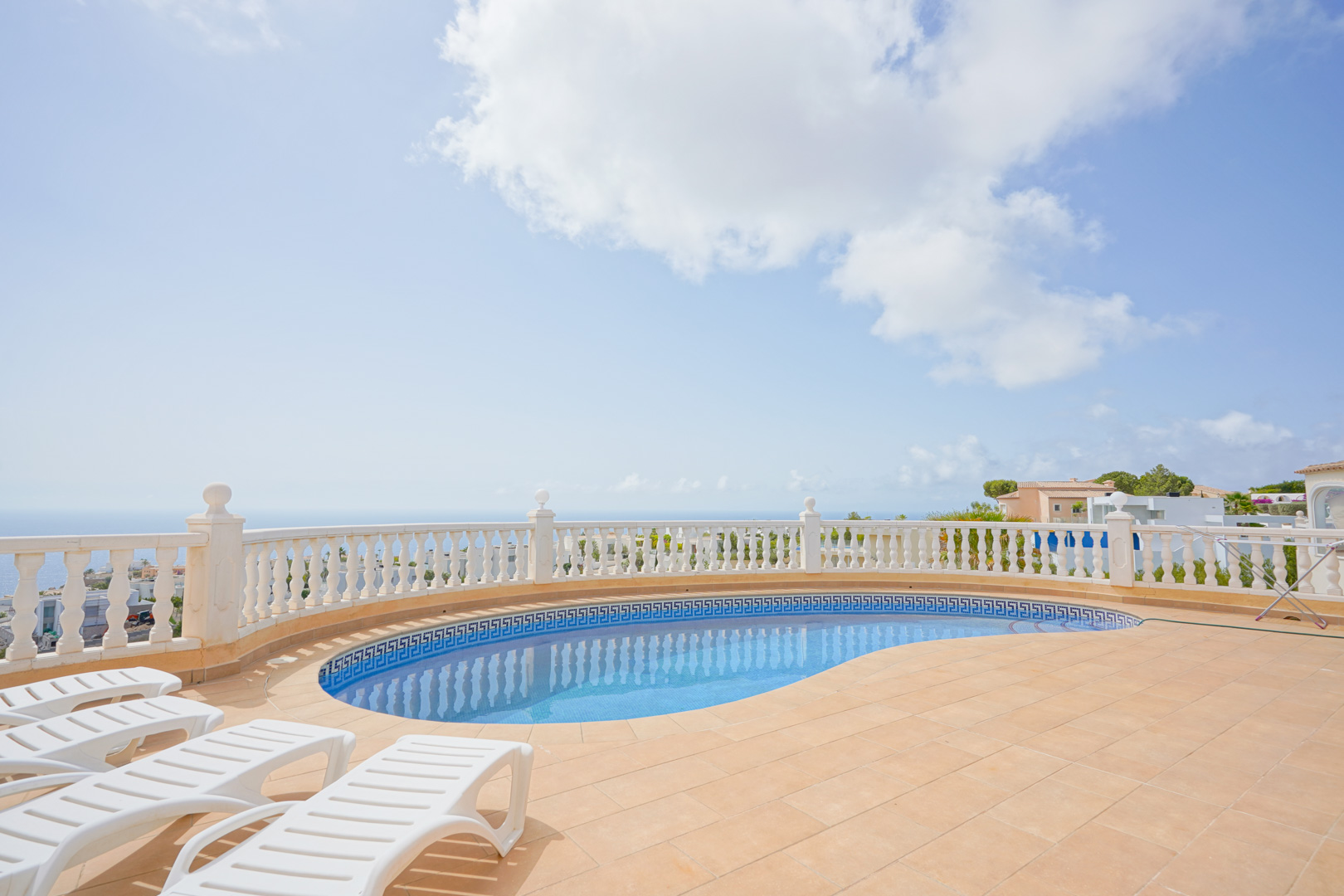 Terrasse avec piscine incurvée, balustrade blanche et vue panoramique sur la Méditerranée, équipée de chaises longues sur carrelage.