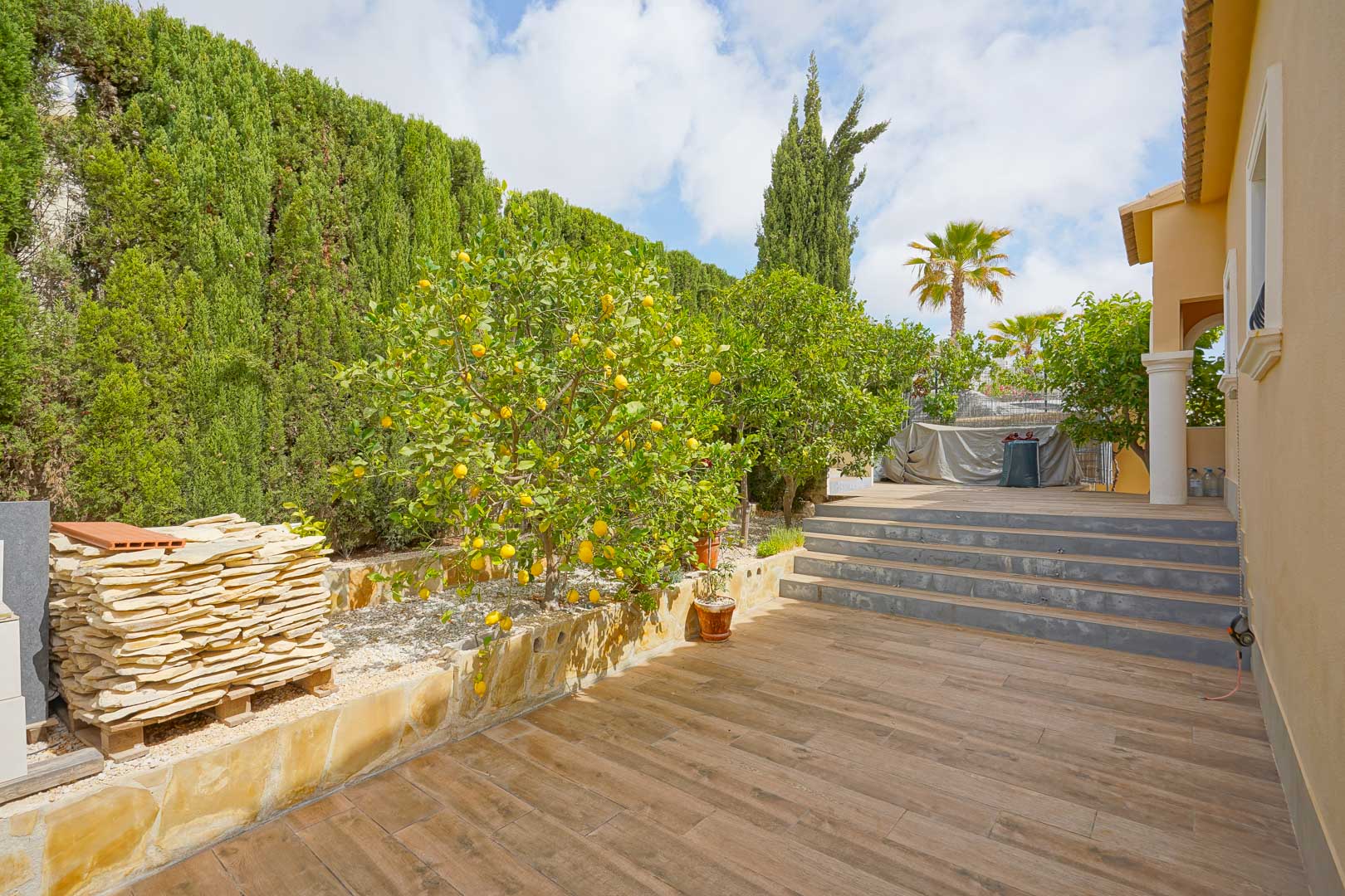 Terrasse extérieure avec carrelage imitation bois, bordée de citronniers et de hautes haies de cyprès, avec des marches reliant les niveaux du jardin.
