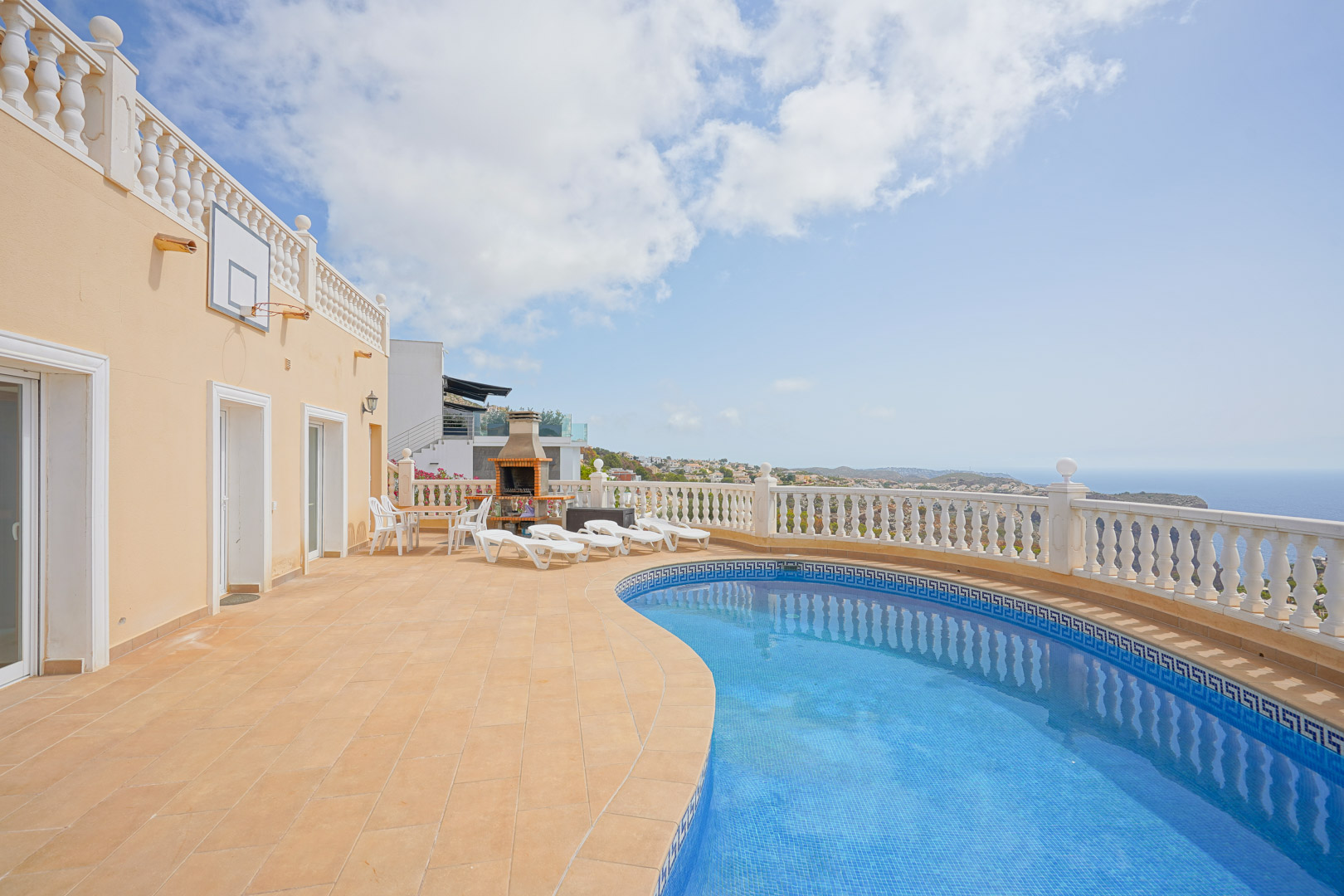 Terrasse extérieure avec piscine de forme libre, barbecue en brique et balustrade blanche offrant une vue panoramique sur la mer Méditerranée et le littoral.