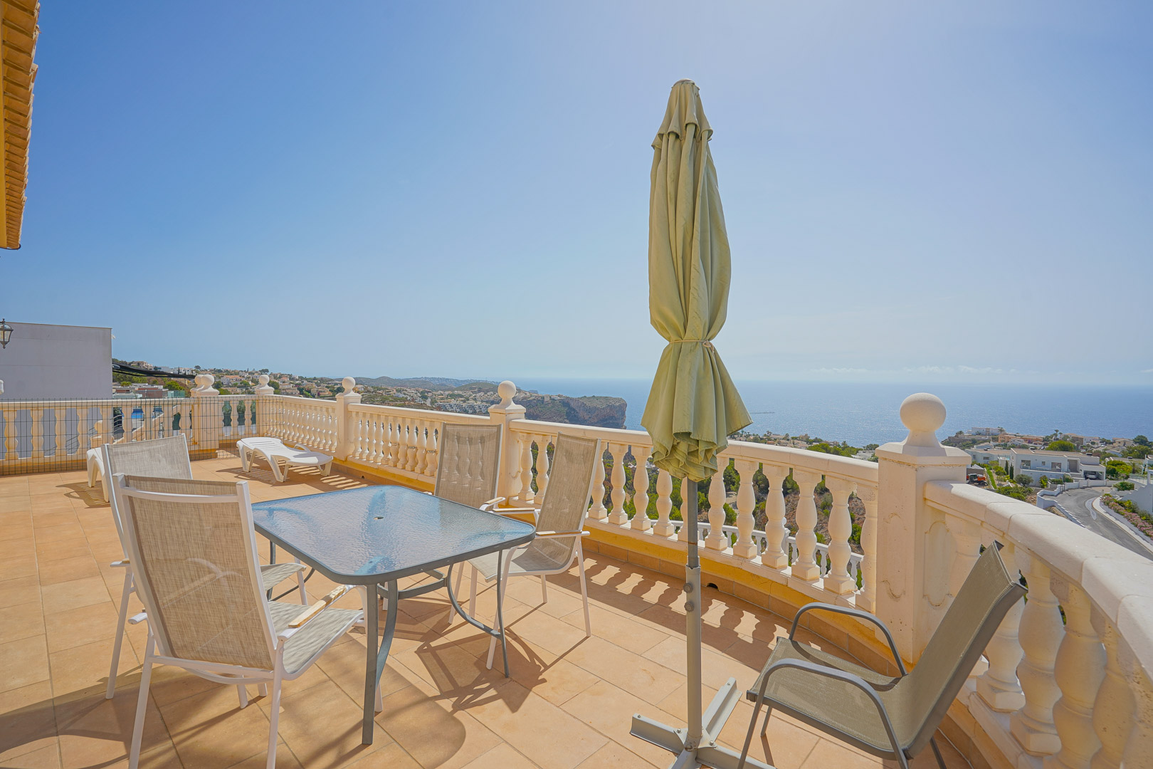 Terrasse supérieure avec table en verre, chaises d'extérieur et balustrade blanche, offrant une vue panoramique sur la mer Méditerranée et les falaises.