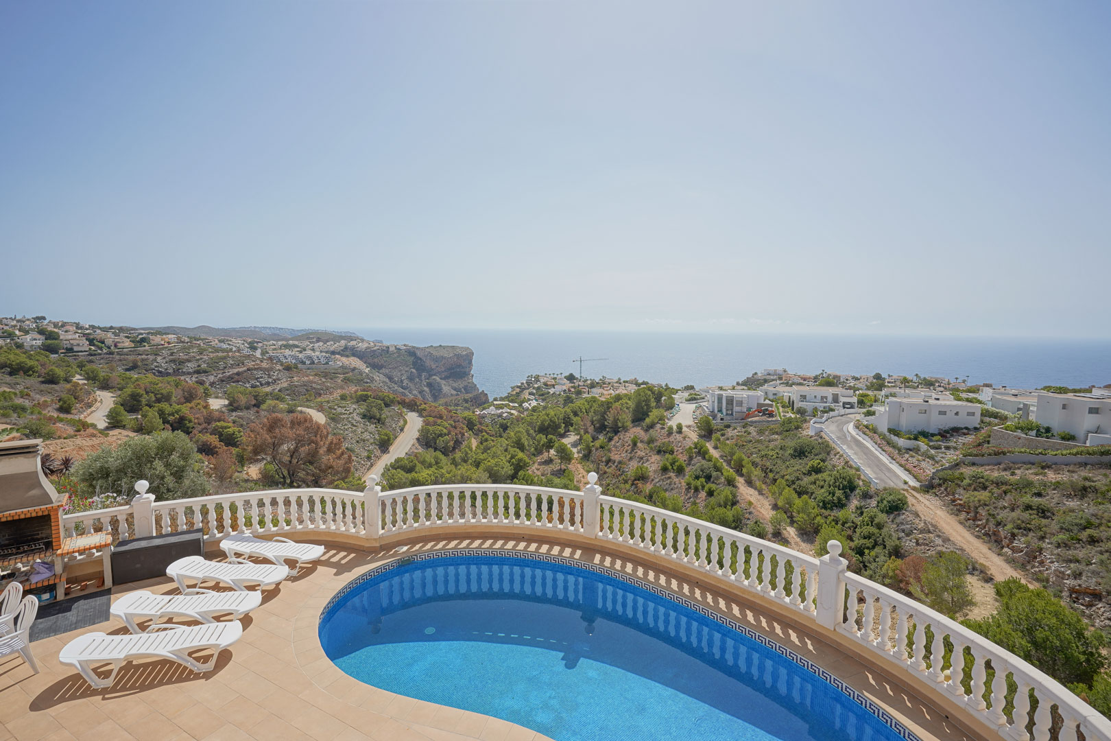 Terrasse surélevée avec piscine en forme de rein, balustrade blanche et barbecue maçonné, offrant une vue panoramique sur la mer Méditerranée et les falaises.