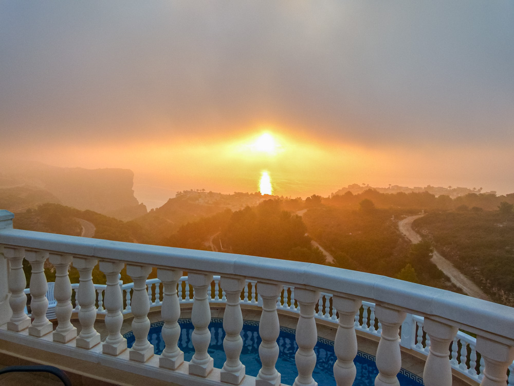 Vue depuis la terrasse avec balustrade blanche sur la piscine et le coucher de soleil doré sur les falaises de Cumbre del Sol.