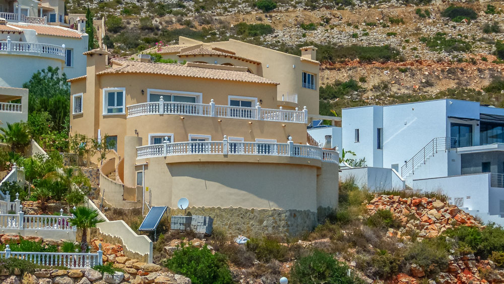 Vue extérieure de la villa de style méditerranéen aux façades ocre, présentant de vastes terrasses incurvées avec balustrades blanches intégrées au relief.