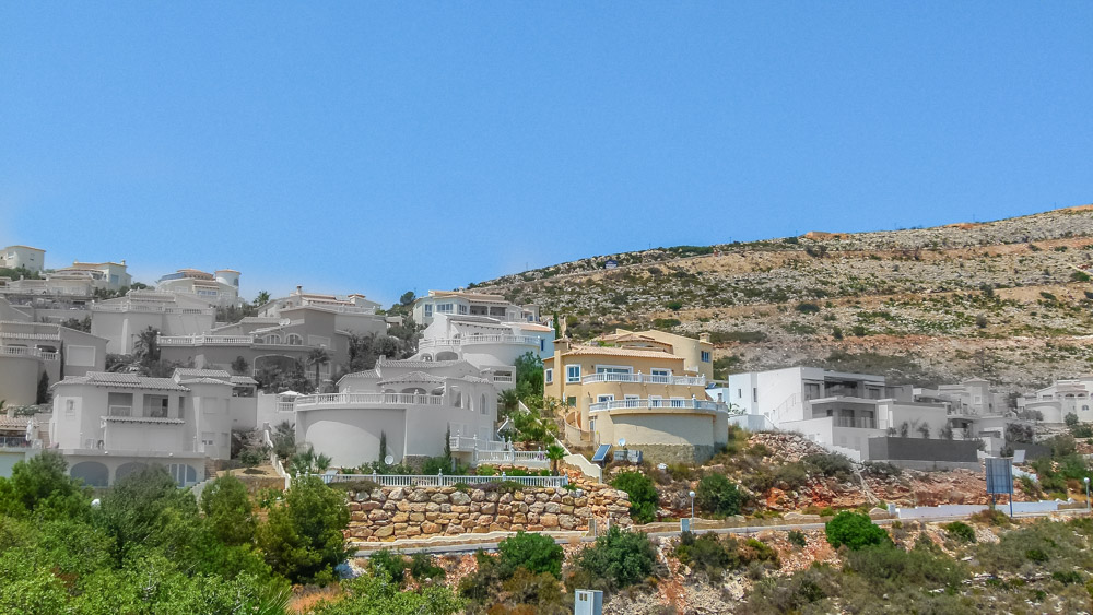 Vue panoramique de villas blanches en terrasses sur la colline de Cumbre del Sol, avec des murs en pierre naturelle et des balustrades classiques.
