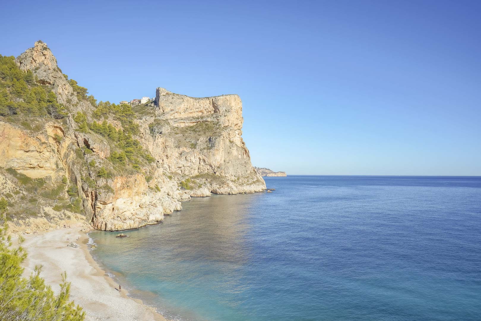 Vue panoramique sur les falaises de Cumbre del Sol et la plage de Cala Moraig, bordées par les eaux turquoise de la Méditerranée sous un ciel azur.