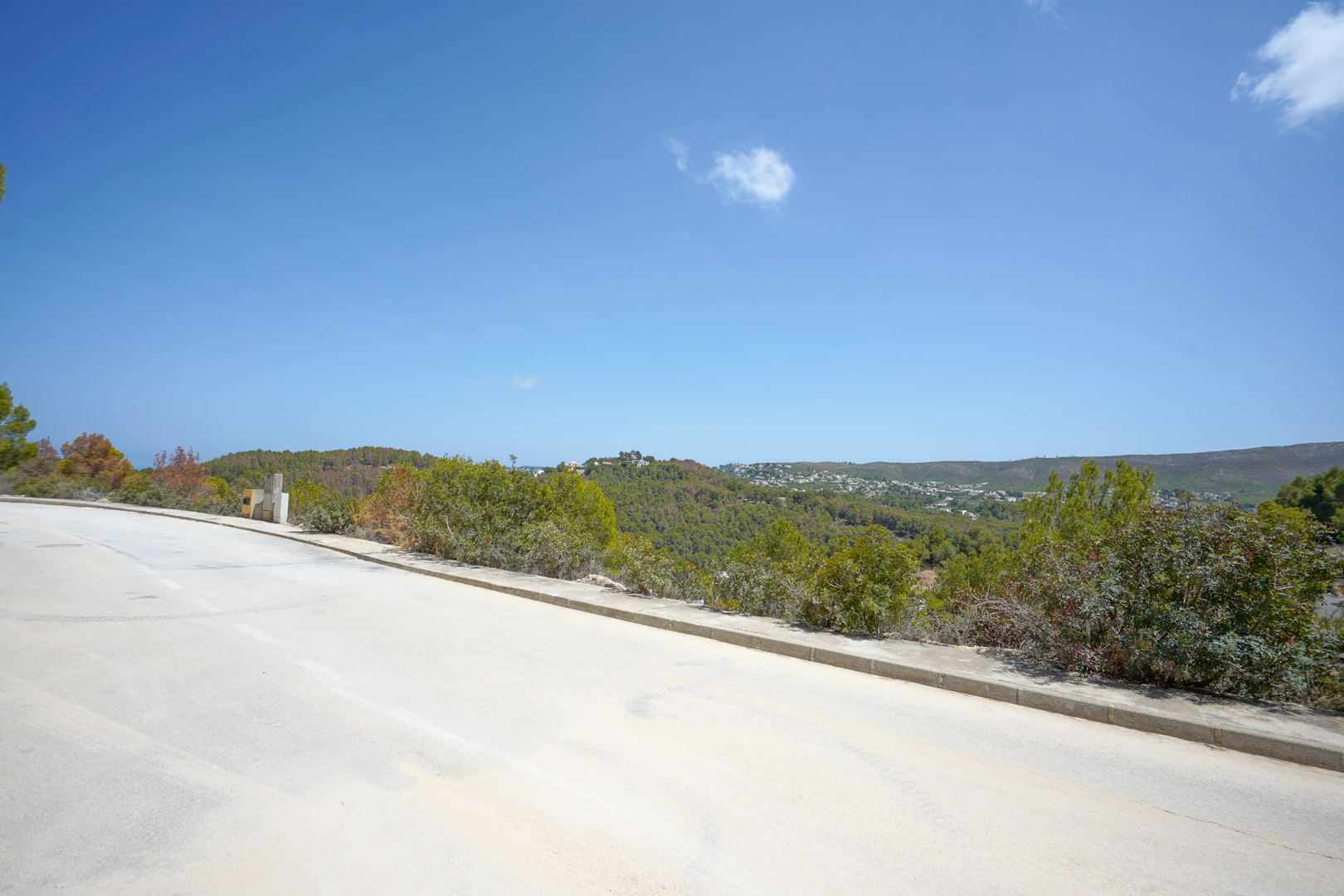 Vue depuis la route goudronnée de l'urbanisation montrant l'accès direct aux terrains et les vues panoramiques sur les collines boisées.
