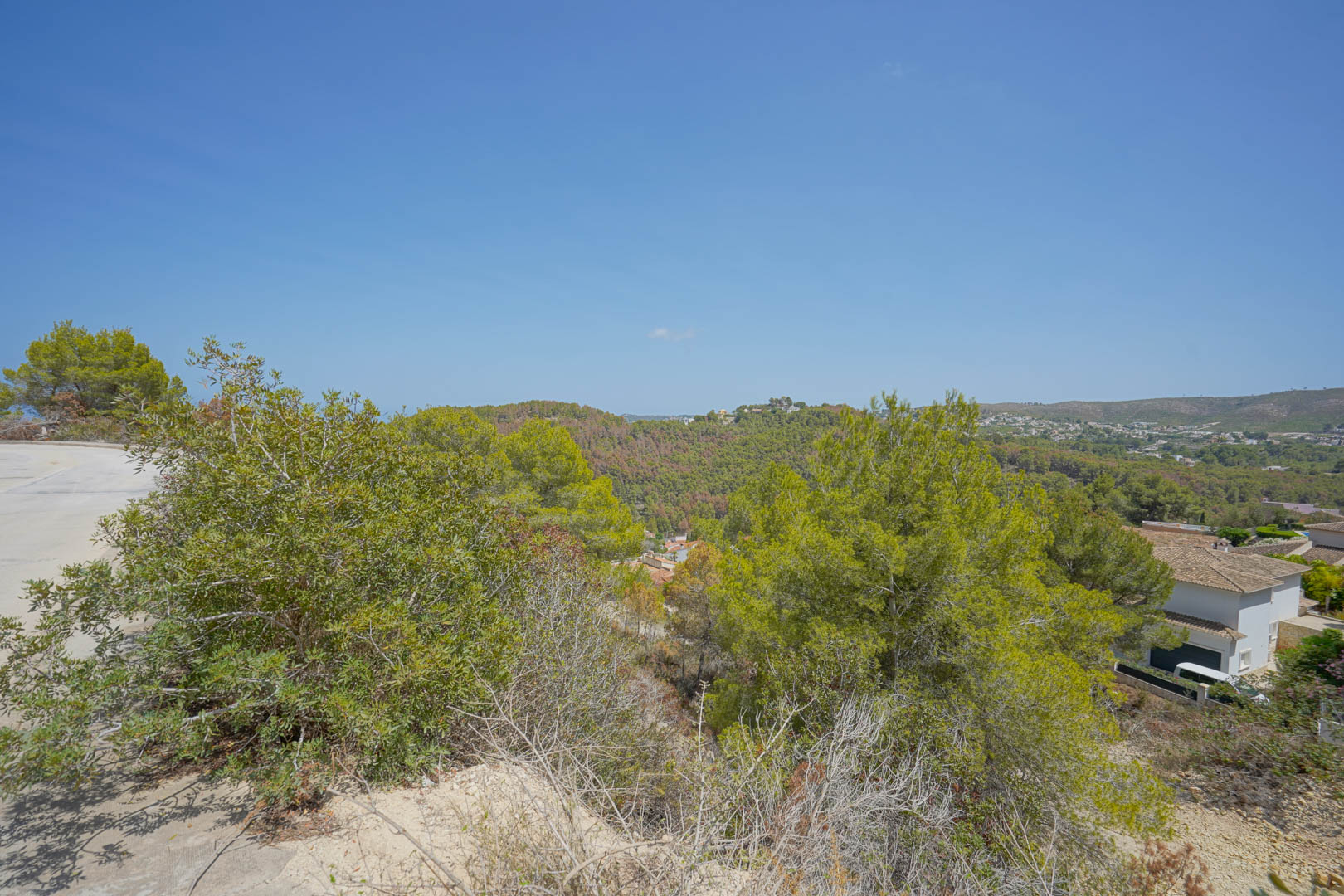 Vue panoramique depuis le terrain en pente montrant la route d'accès goudronnée et les collines verdoyantes environnantes.