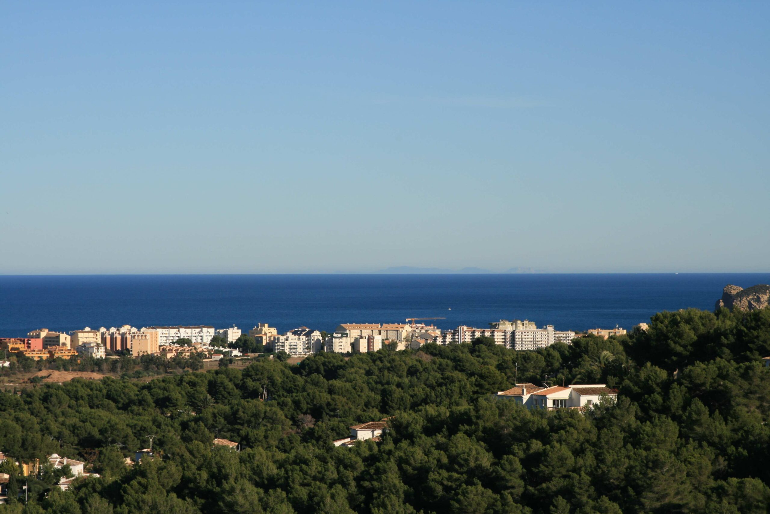 Vue panoramique depuis le terrain surplombant une pinède dense, les bâtiments côtiers et l'horizon bleu de la mer Méditerranée par temps clair.