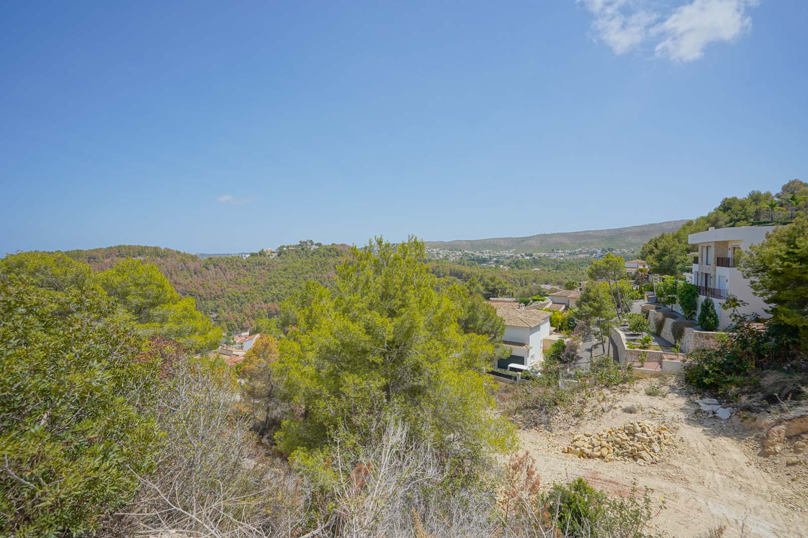Vue panoramique surélevée depuis le terrain, illustrant la topographie naturelle, les pins méditerranéens et les villas voisines avec l'horizon marin au loin.