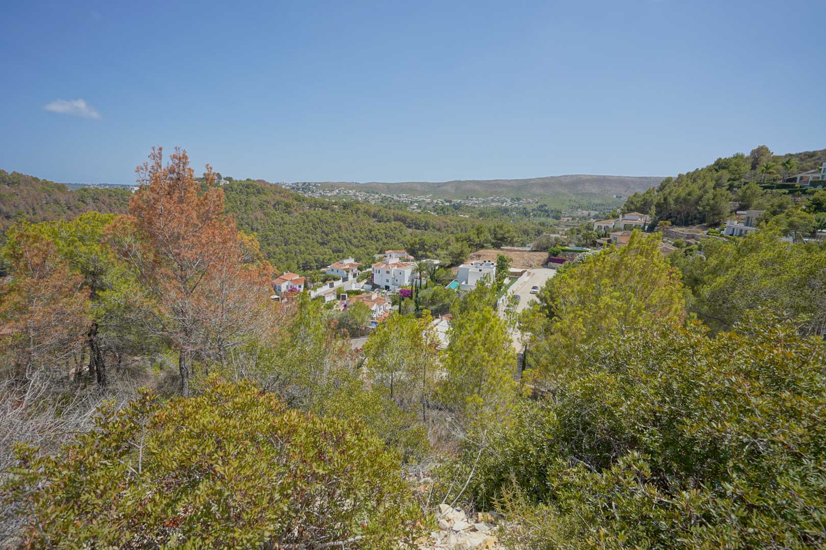 Vue surélevée depuis le terrain dominant la vallée, avec une végétation méditerranéenne dense et des villas blanches réparties sur les collines environnantes.