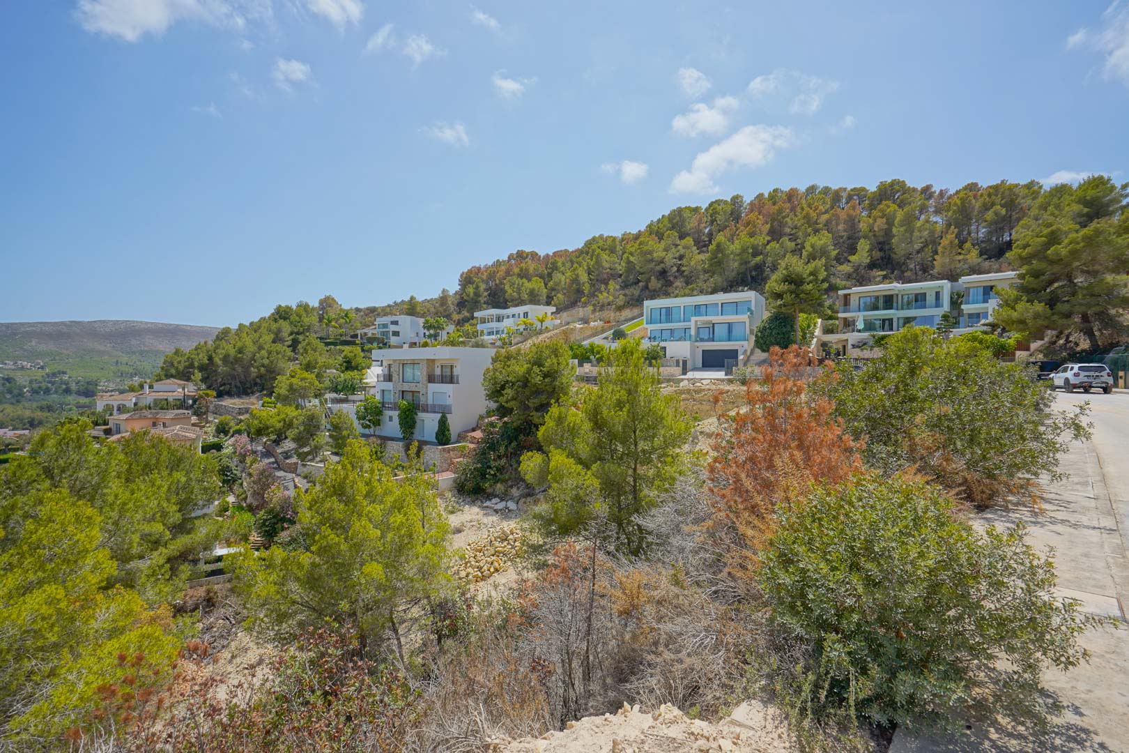 Vue surélevée du quartier résidentiel montrant des villas modernes intégrées à la pente naturelle, entourées d'une végétation méditerranéenne.