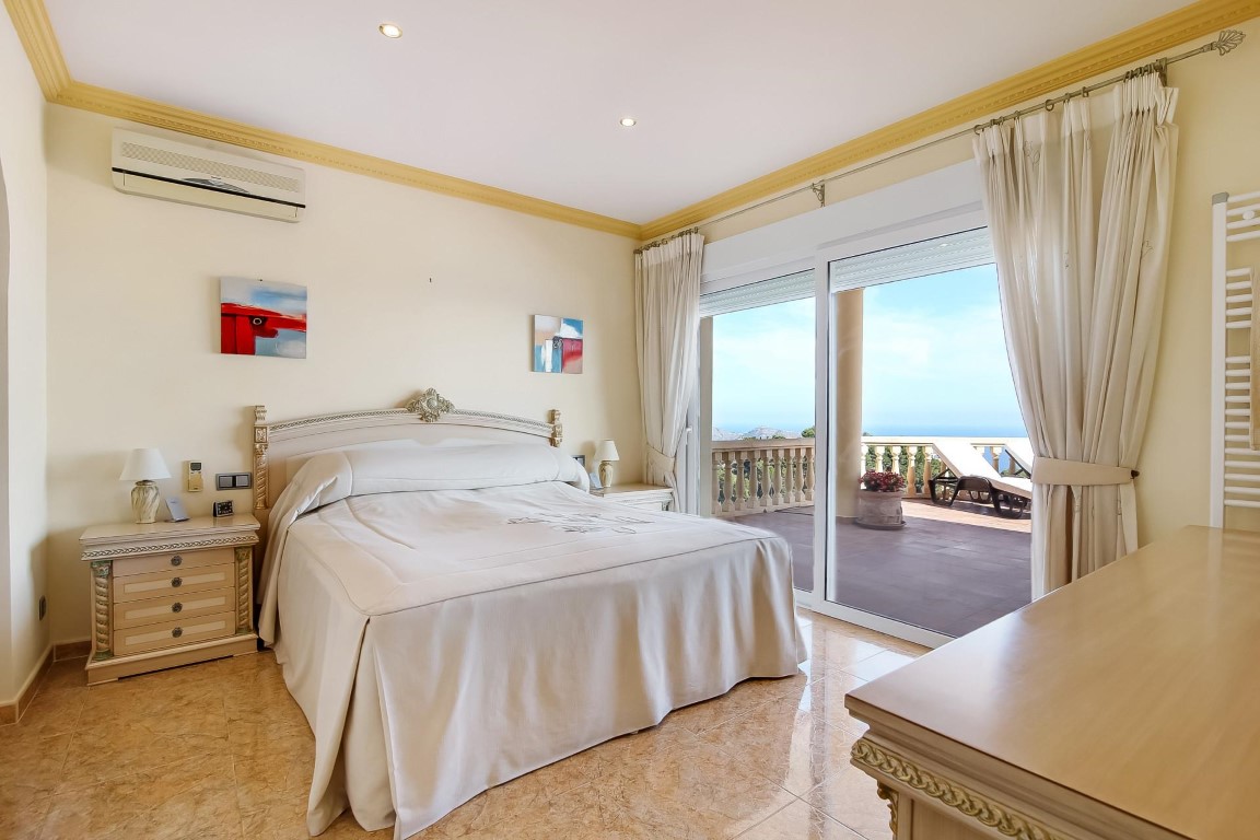Chambre principale avec accès à la terrasse, sol en grès, climatisation et grandes baies vitrées offrant une vue dégagée sur la mer Méditerranée.