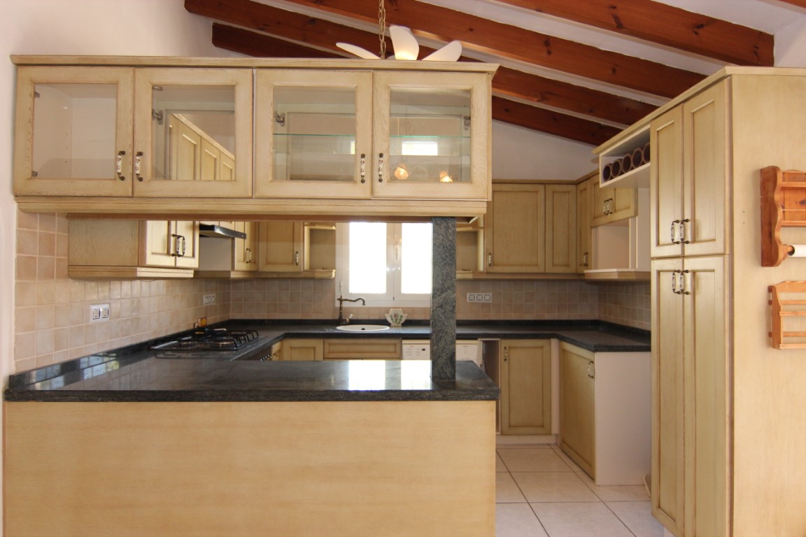 Cuisine de style rustique avec poutres en bois apparentes, plans de travail en granit noir et meubles clairs avec vitrines intégrées et bar de service.