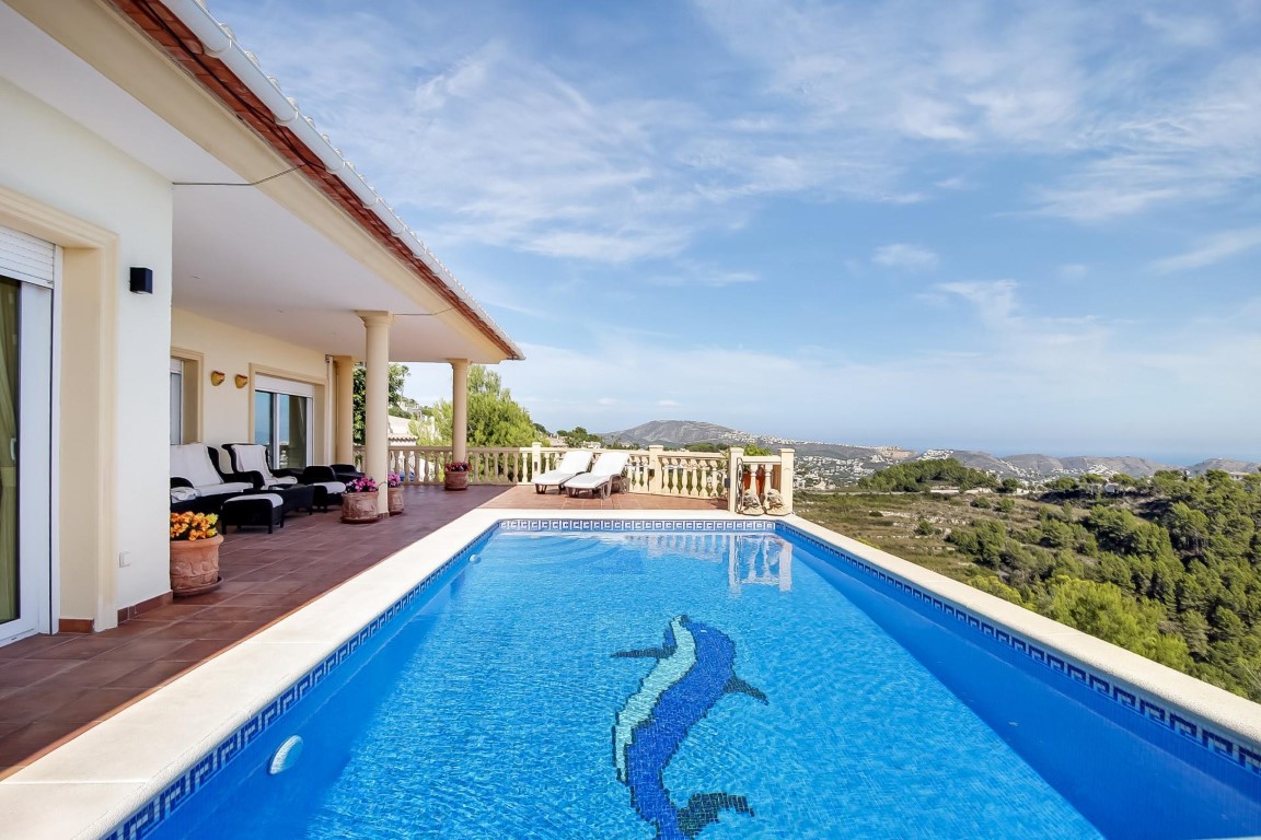 Piscine extérieure avec mosaïque de dauphin et terrasse en terre cuite, offrant une vue panoramique sur la mer et les collines environnantes de Moraira.