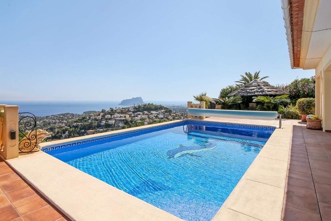 Piscine extérieure avec mosaïque de dauphin et vue panoramique sur la mer Méditerranée et le Peñón de Ifach, entourée d'une terrasse en terre cuite.