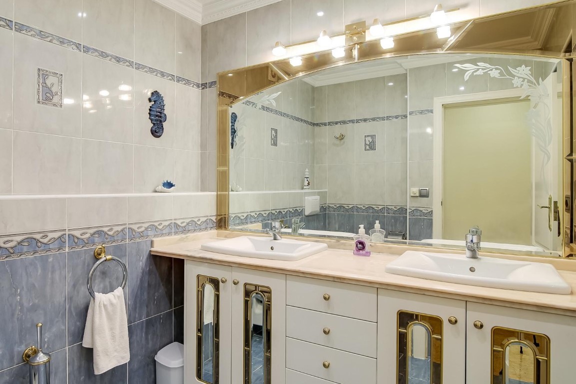 Salle de bain principale avec double vasque, plan de travail en marbre, meubles aux finitions dorées et carrelage mural décoratif bleu et blanc.