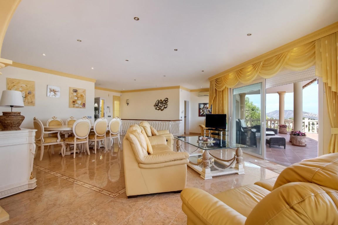 Salon-salle à manger ouvert avec sols en grès poli, mobilier classique de couleur crème et accès direct à une terrasse offrant une vue dégagée.