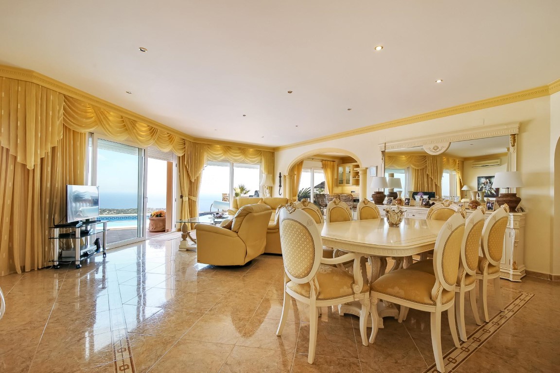 Salon-salle à manger spacieux avec sols en marbre, mobilier classique et grandes baies vitrées offrant une vue panoramique sur la mer Méditerranée.