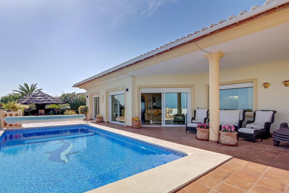 Terrasse principale avec piscine à mosaïque, porche couvert soutenu par des colonnes et coin salon. Un gazebo au toit de chaume complète l'espace extérieur paysager.