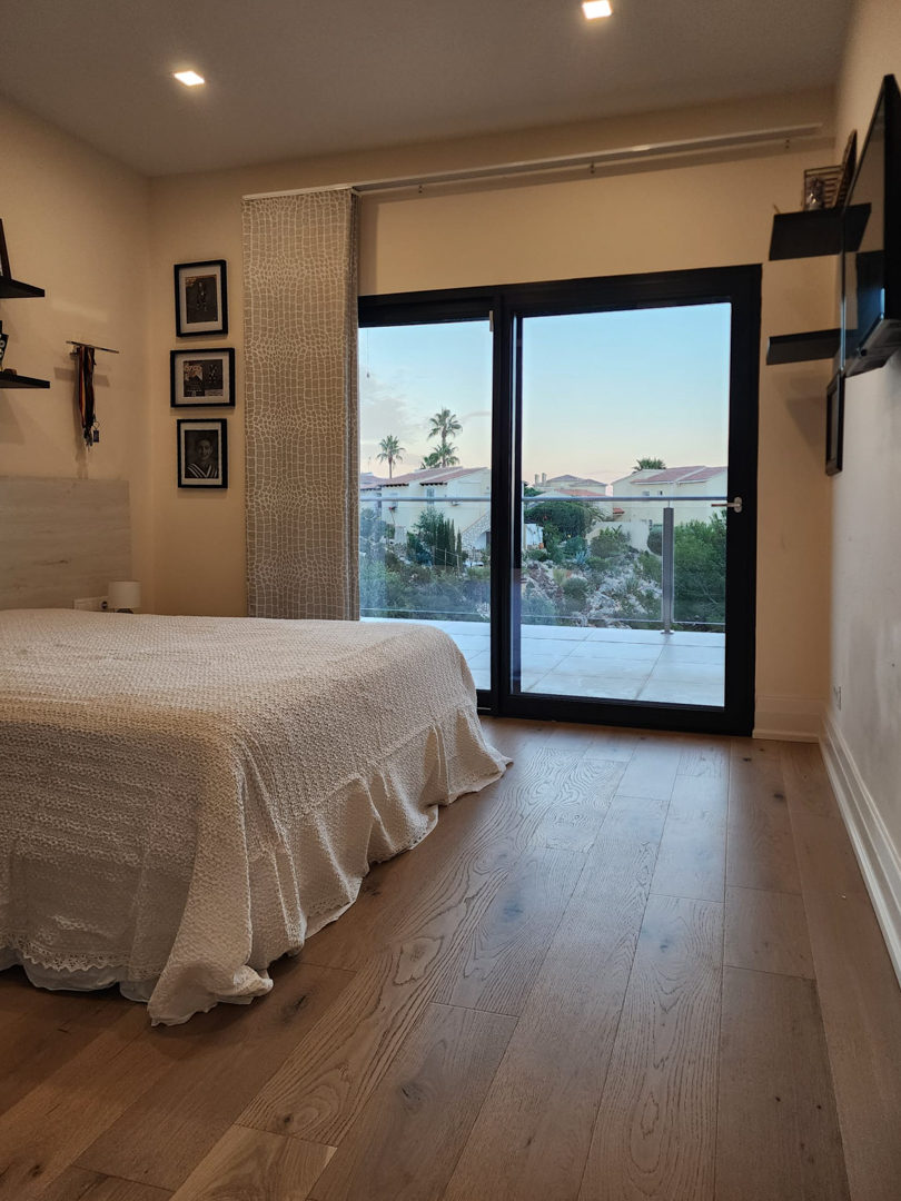 Chambre avec parquet au sol, éclairage encastré et grandes baies vitrées coulissantes offrant un accès direct à une terrasse privée et une vue dégagée.