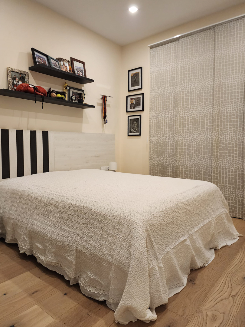 Chambre avec parquet en chêne clair, tête de lit personnalisée et étagères murales. Elle intègre des rideaux à panneaux et un éclairage encastré.