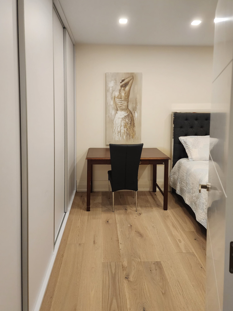 Chambre avec placards intégrés du sol au plafond, un espace bureau en bois et un parquet en chêne sous des spots encastrés au plafond.