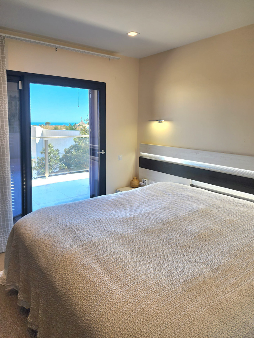 Chambre lumineuse avec tête de lit à éclairage LED intégré et accès direct à la terrasse offrant une vue panoramique sur la mer.