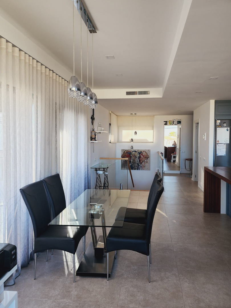 Coin repas lumineux avec table en verre, chaises en cuir noir et suspensions design, situé près de grandes fenêtres et de l'escalier avec garde-corps en verre.